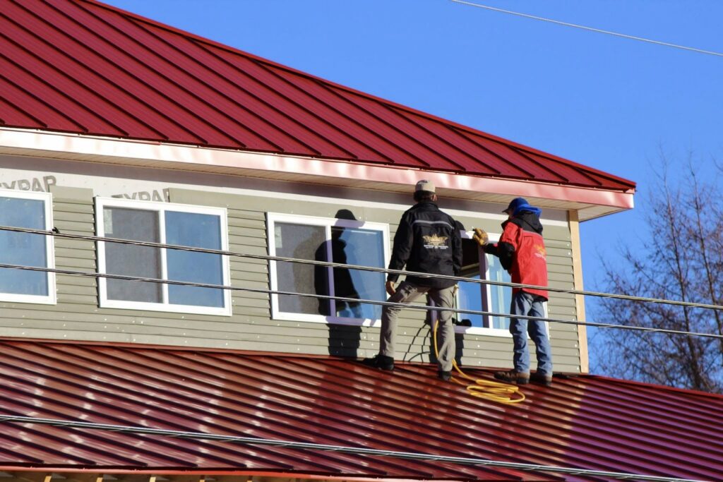 A pair of contractors stand atop the new Gallerie's red tin roof, glancing through the top-floor windows of the soon-to-be Archival Library.