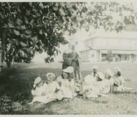 A Sister of the Mont-Carmel convent school with a group of children at rest within the shade of a tree.