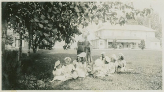 A Sister of the Mont-Carmel convent school with a group of children at rest within the shade of a tree.